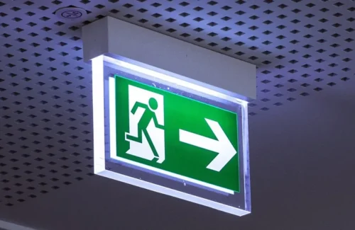 Leuchtendes Rettungswege-Schild an Decke mit kleinen quadratischen Löchern.