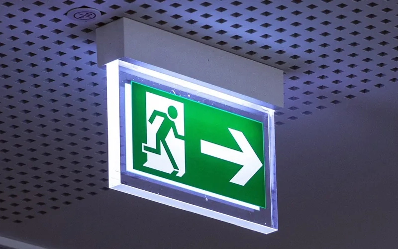 Leuchtendes Rettungswege-Schild an Decke mit kleinen quadratischen Löchern.